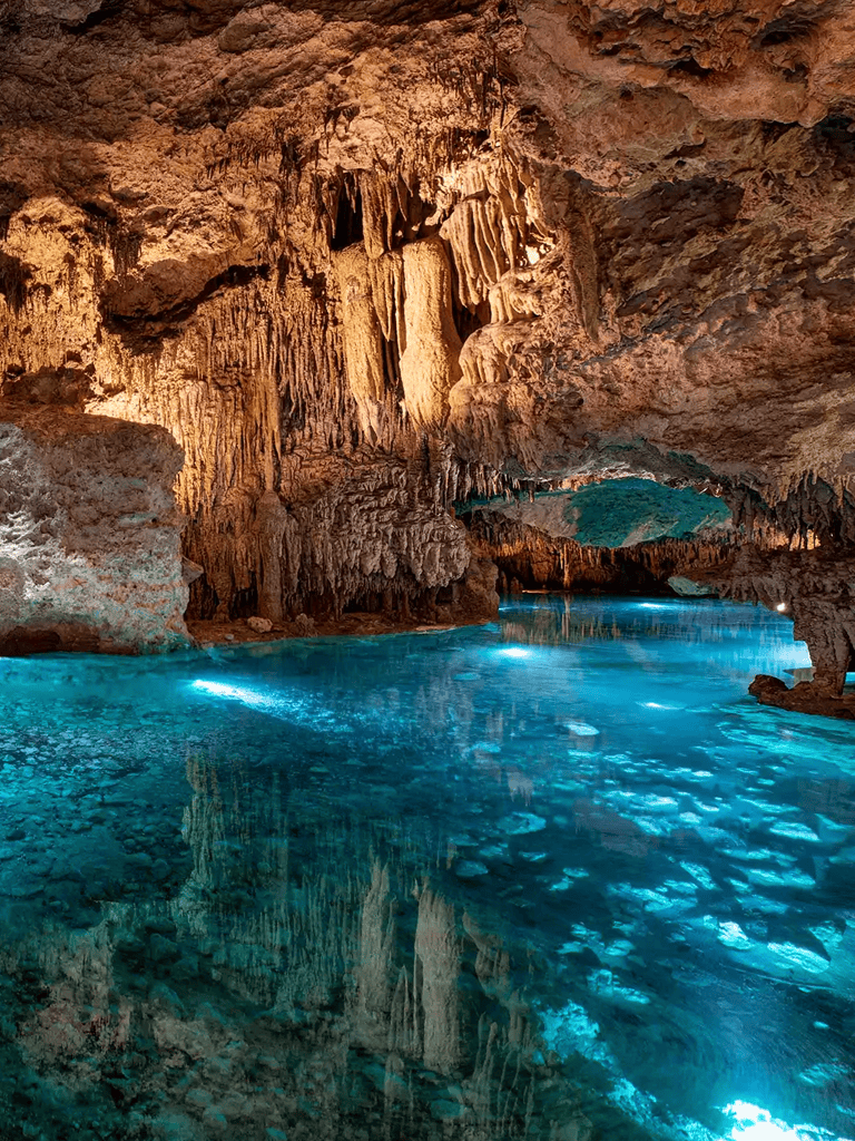 Hidden cave with stalactites and stalagmites illuminated by blue water in Quest For Directions cavern.