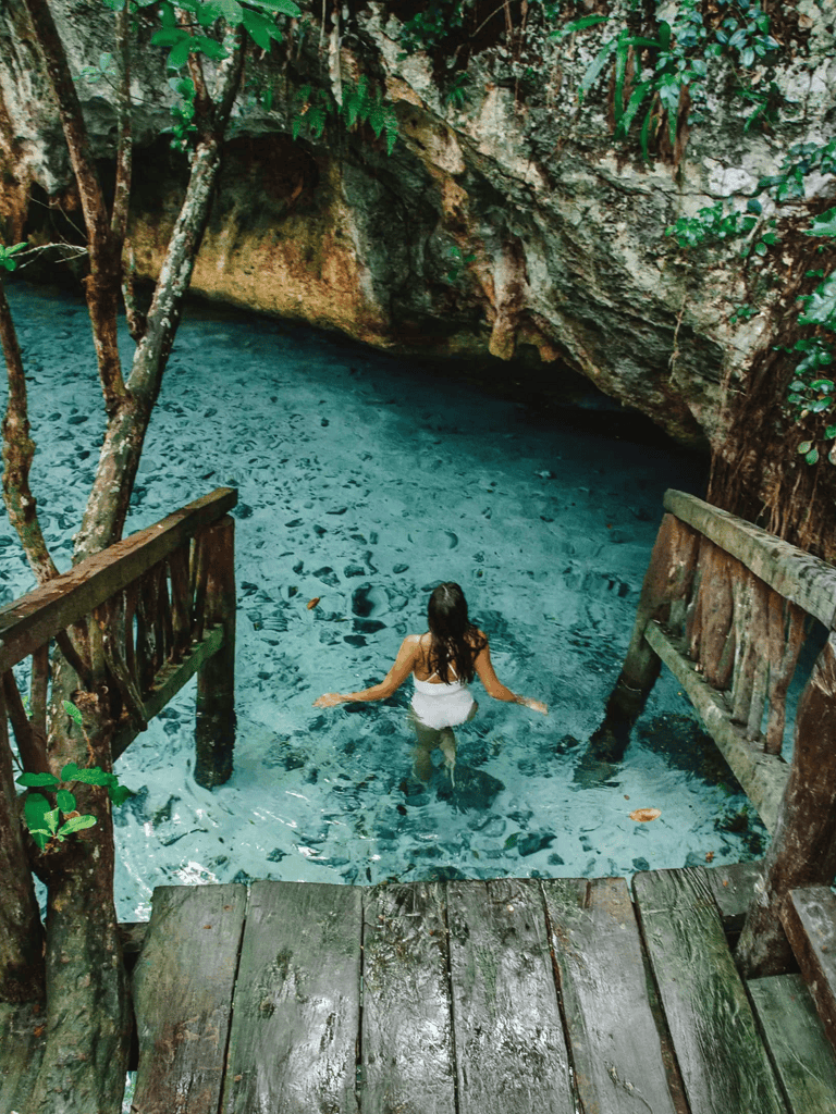 Serene woman swimming in natural cenote surrounded by lush jungle vegetation.