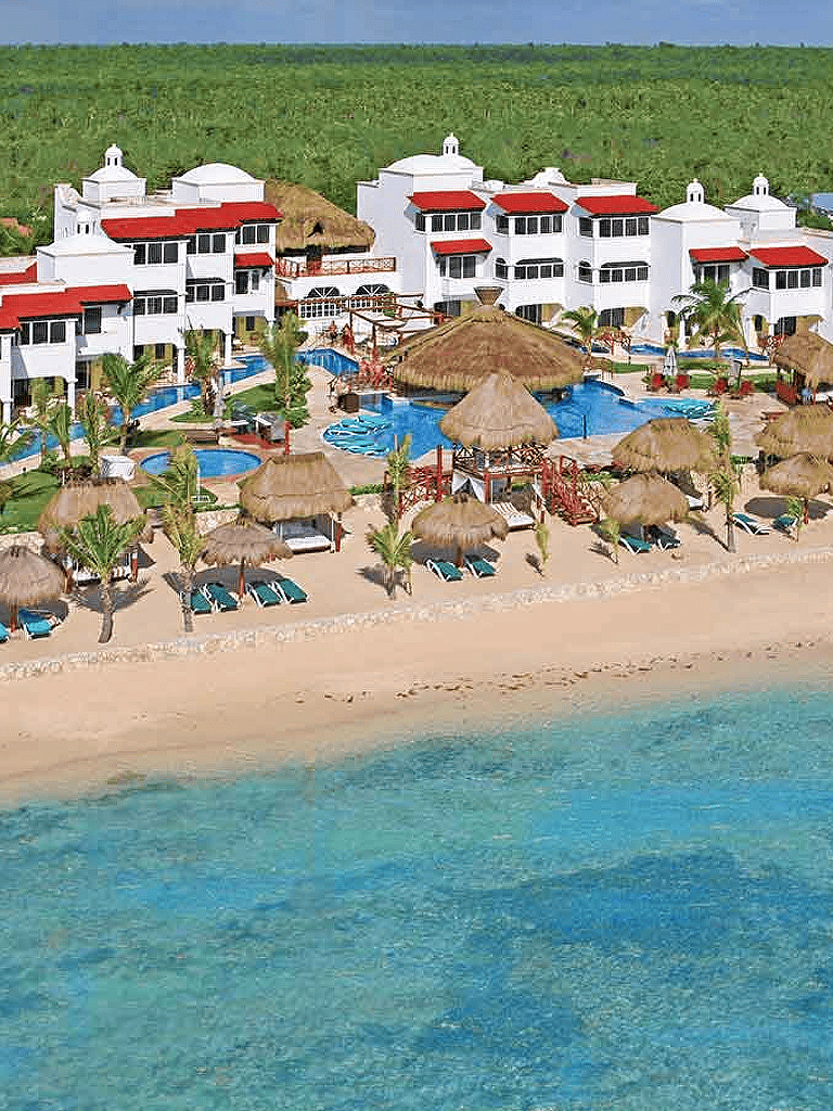 Elegant seaside resort with white buildings, swimming pools, and tropical thatched-roof cabanas by the beach.
