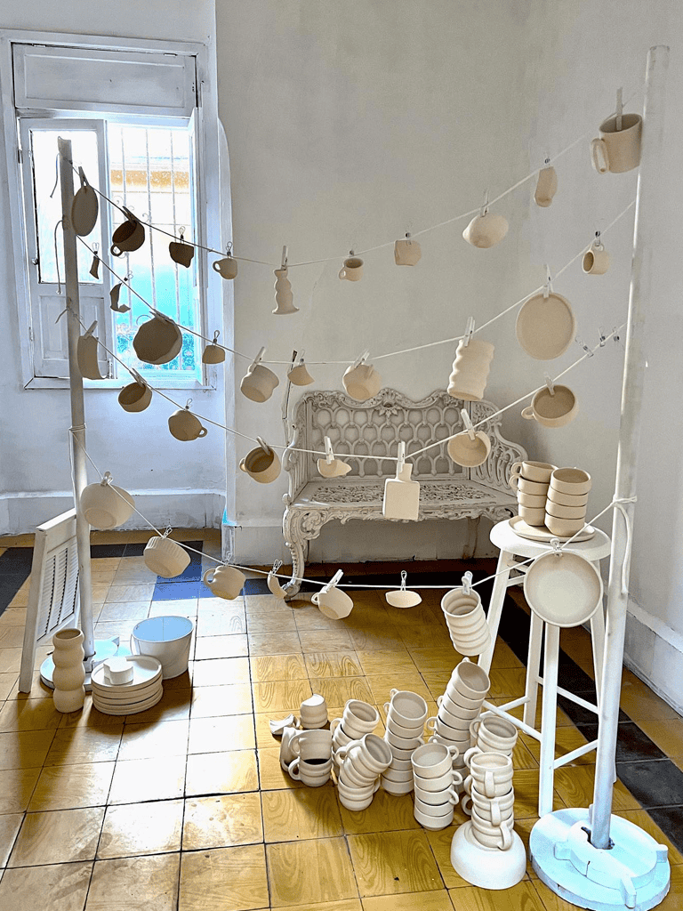 Clay pottery display with cups and plates, decorative white furniture, cozy indoor setting, artisanal ceramics, QuestForDirections.