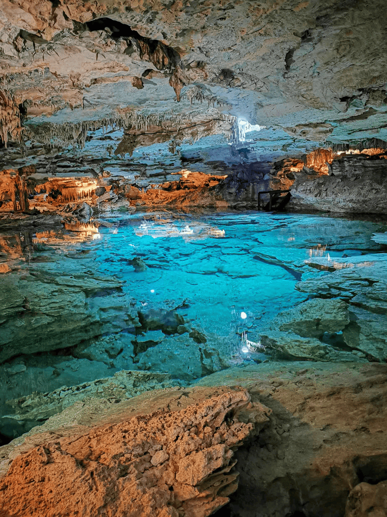 Crystalline cave with colorful lighting, underground formations, and clear water pool.