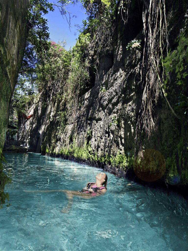 Tranquil woman swimming in blue water canyon with lush greenery and rock walls, adventure and nature exploration.
