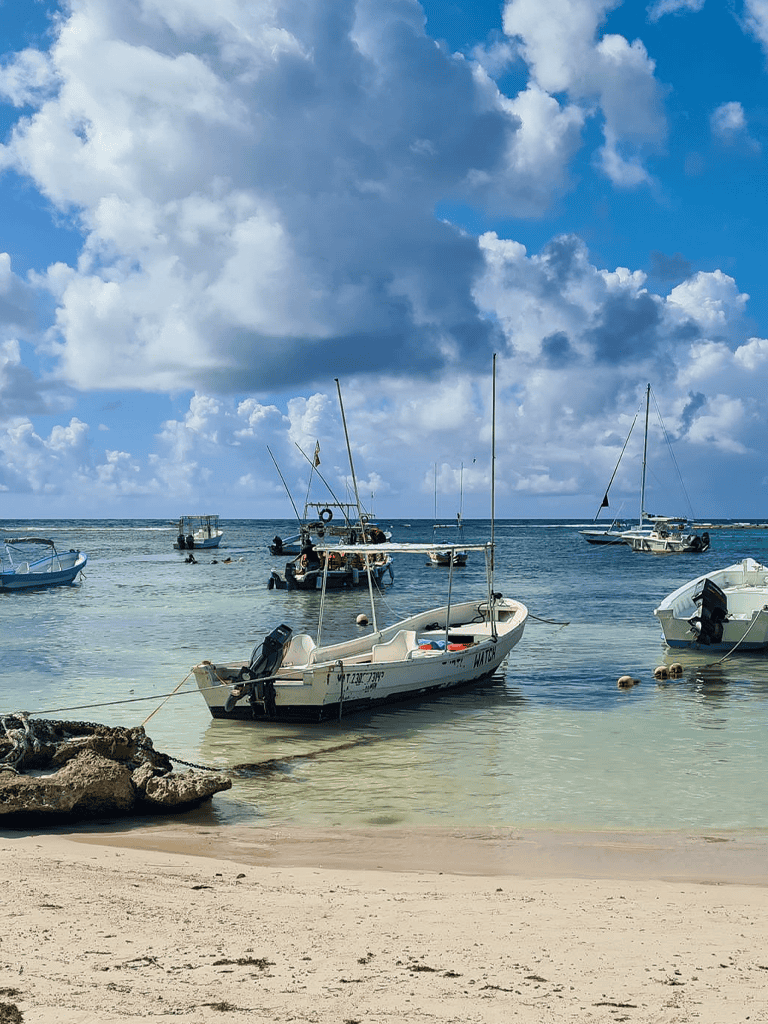 Boats anchored on clear beach waters with sky and clouds in background.