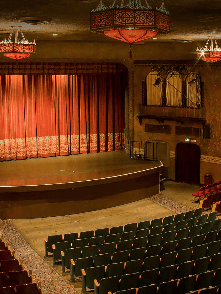A cozy theater stage with red curtains and vintage lighting, perfect for live performances and cultural events.