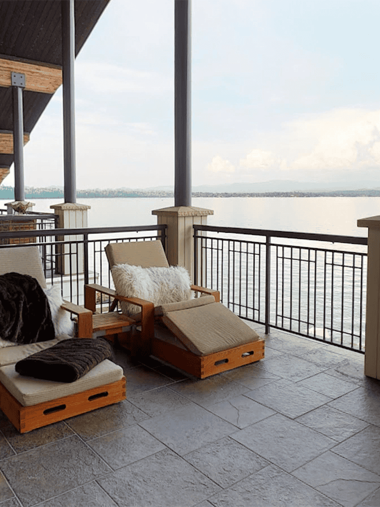 Serene lakeside balcony with cozy lounge chairs and picturesque water view, perfect for relaxation.