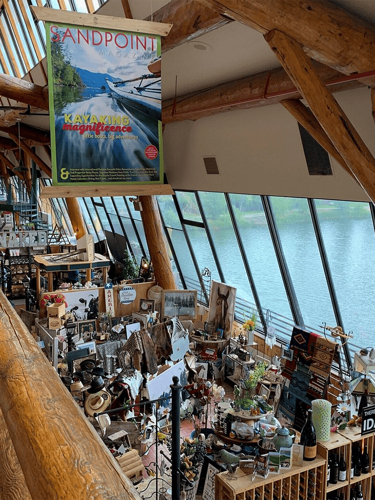 Vibrant indoor market scene with waterfront views and eclectic displays of art, home décor, and unique treasures.