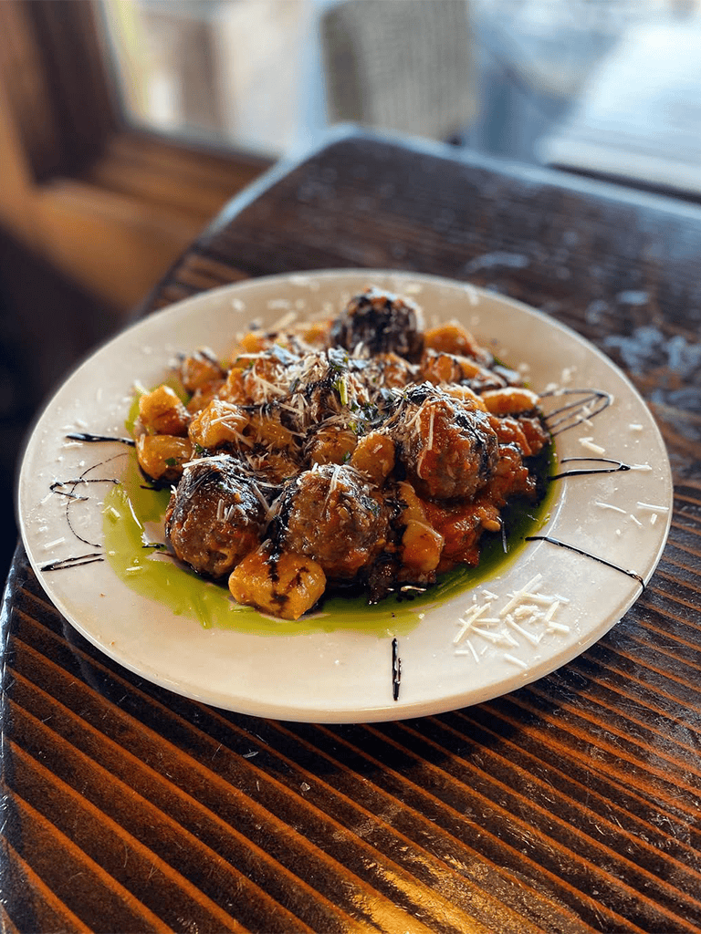 Delicious meatball dish with herbs and sauce on a white plate.