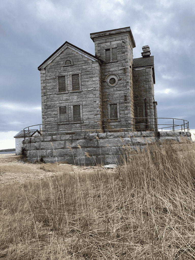 Historic stone lighthouse on grassy coastal landscape under cloudy sky.