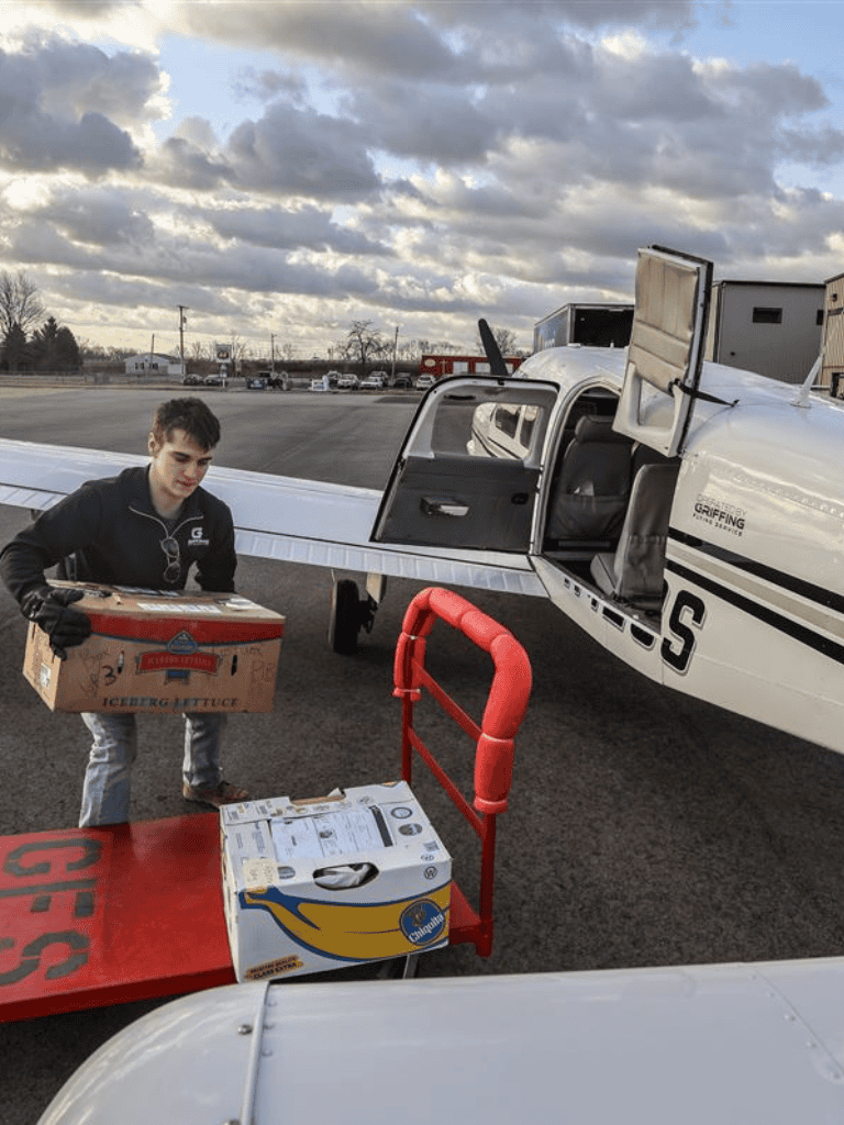 Loading supplies into a small airplane at an airport tarmac.