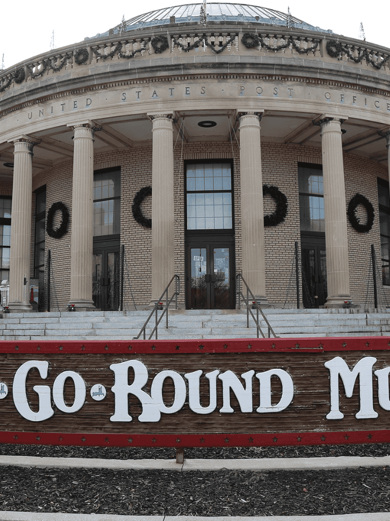 United States Post Office building with decorative wreaths and "G.O. ROUND" sign in front.