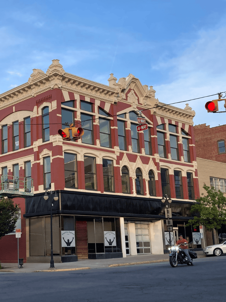 House with classic architectural details in downtown cityscape, featuring cafes, street signs, and a motorcycle.