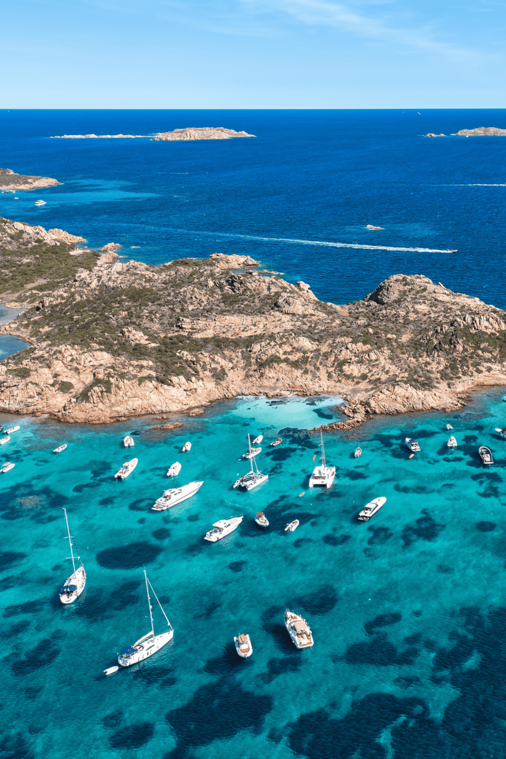 Breathtaking aerial view of turquoise waters, boats, and rocky islands on a sunny day.