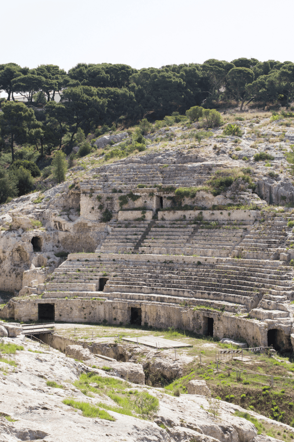 Ancient Greek theater ruins surrounded by lush greenery and rocky terrain, showcasing historical architecture and archaeological significance.