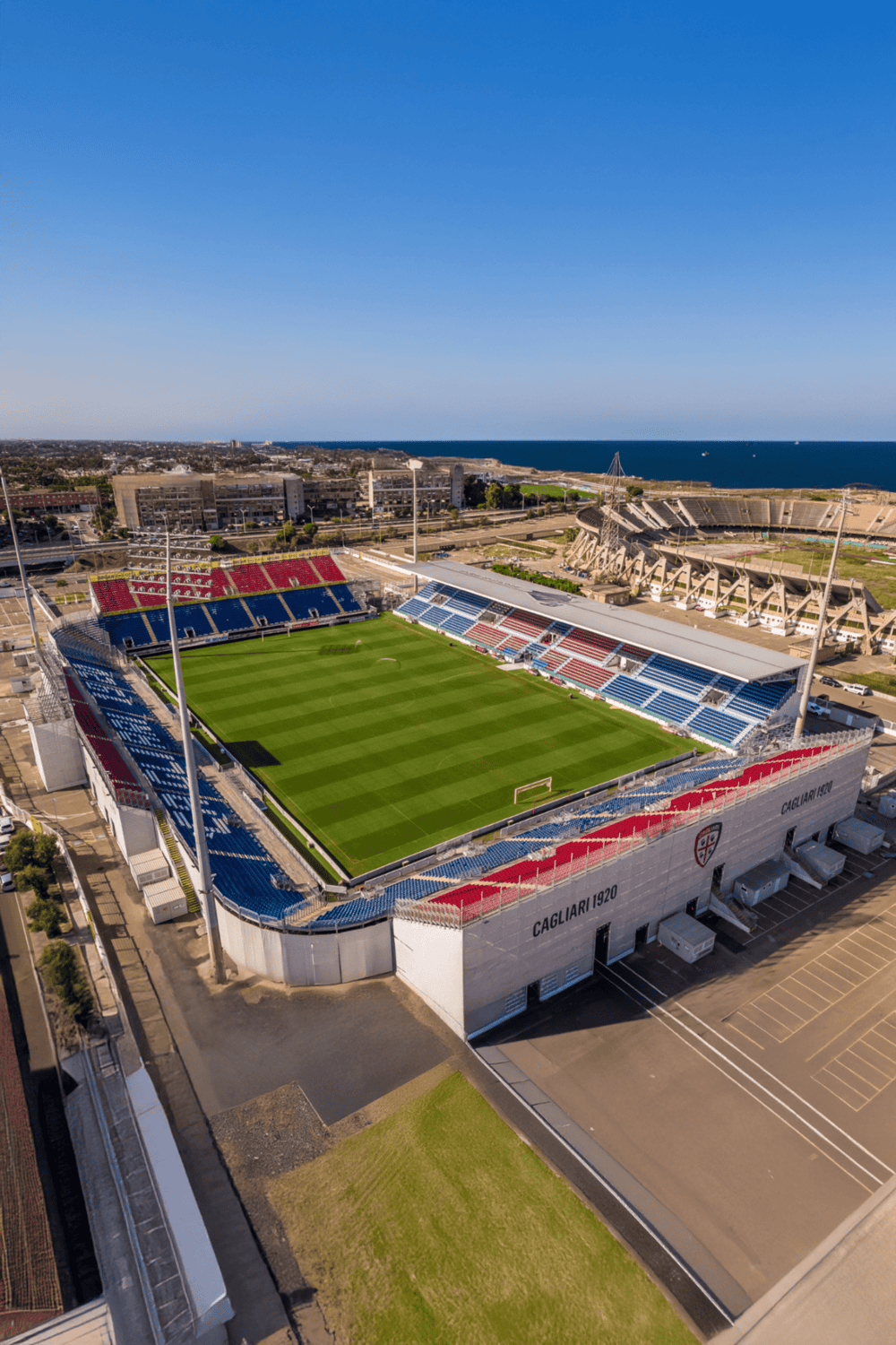 Aerial view of Cagliari stadium in Sardinia with blue sky and ocean backdrop.