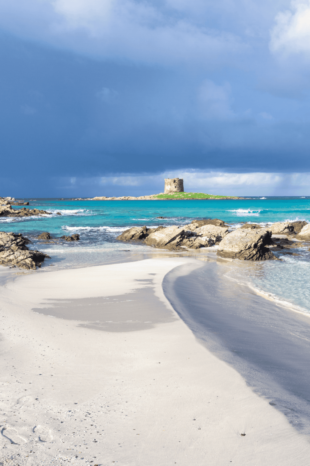 Serene coastal scene with white sandy beach, turquoise waters, and a historic stone tower under a cloudy sky.