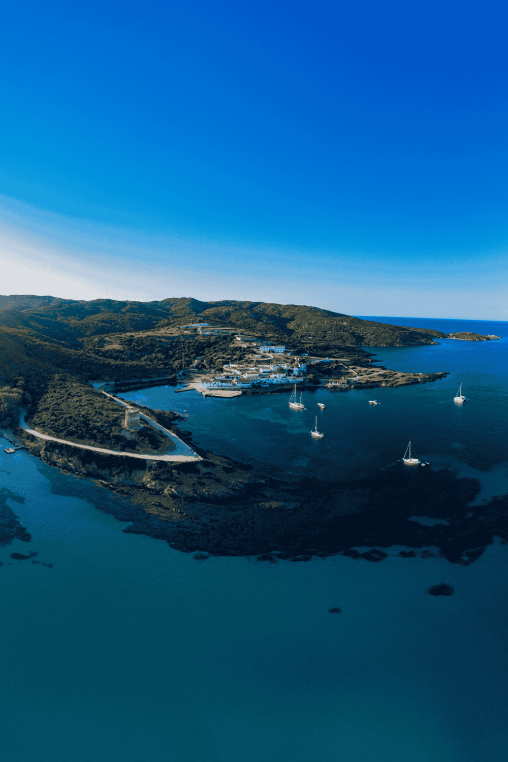 Tranquil island harbor with sailboats and scenic coastline under clear blue sky.