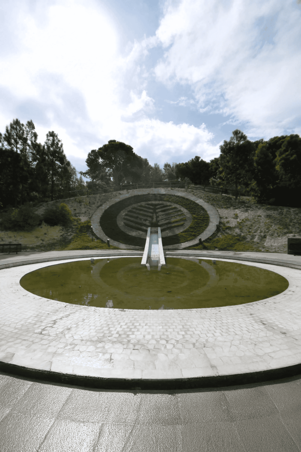 Modern landscape sculpture with a slide, green plants, and trees in the background.