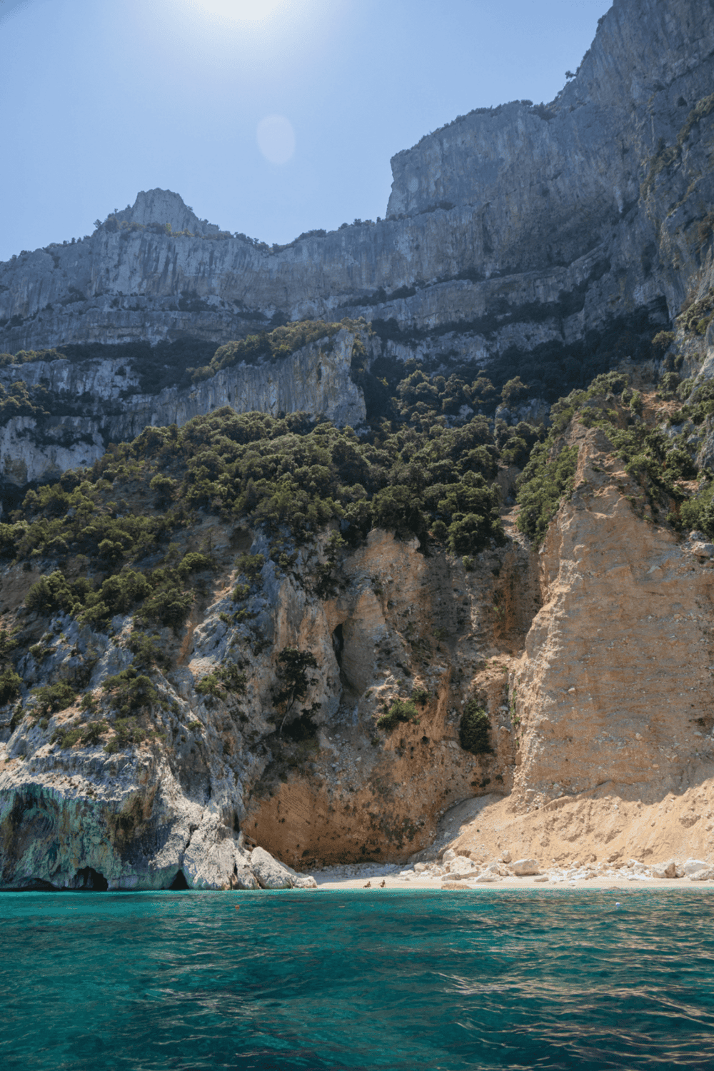 Steep mountain landscape with rocky cliffs, lush greenery, and a clear blue sea, ideal for adventure travel and nature exploration.