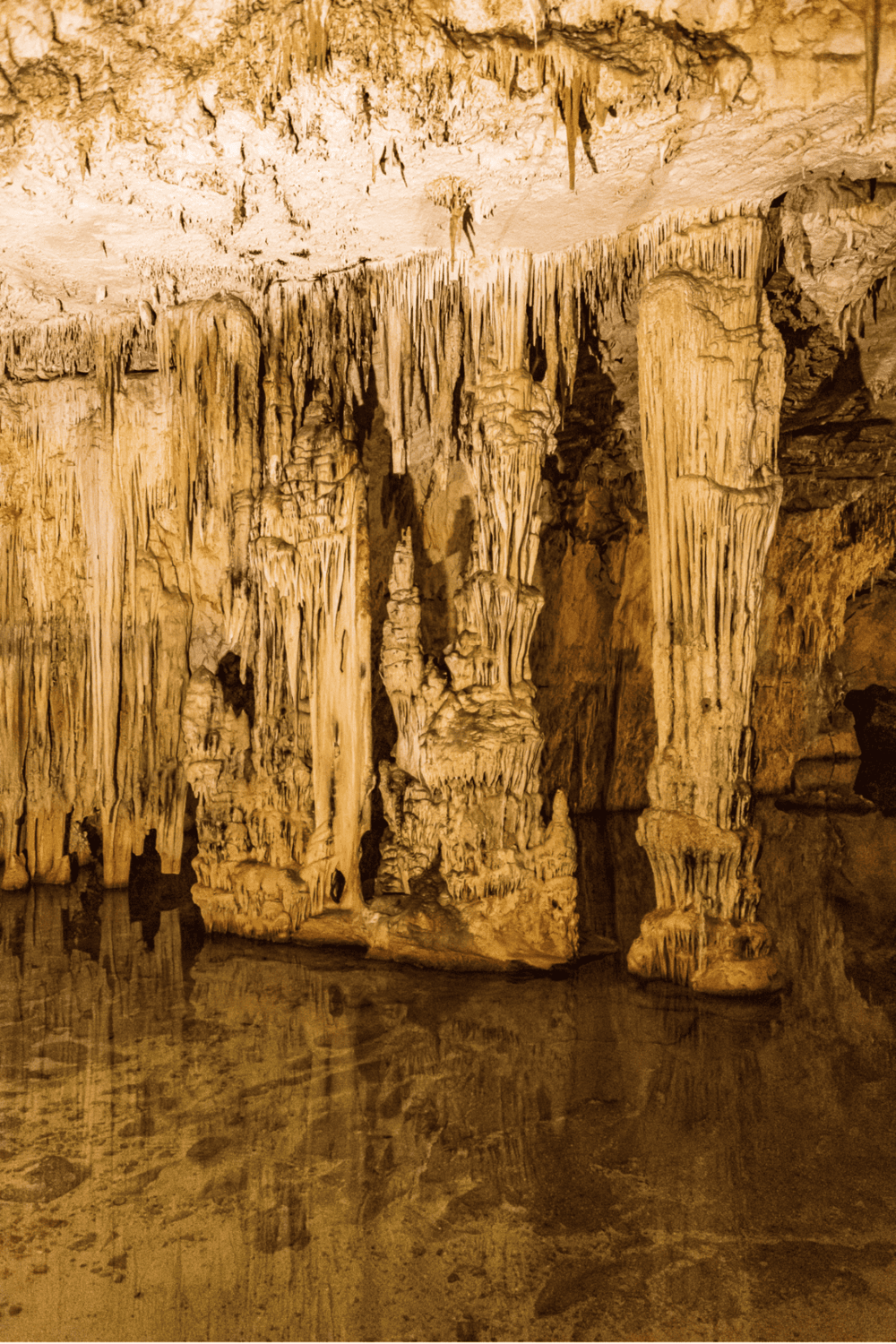 Stalactites and stalagmites in a cave interior with reflection in water.