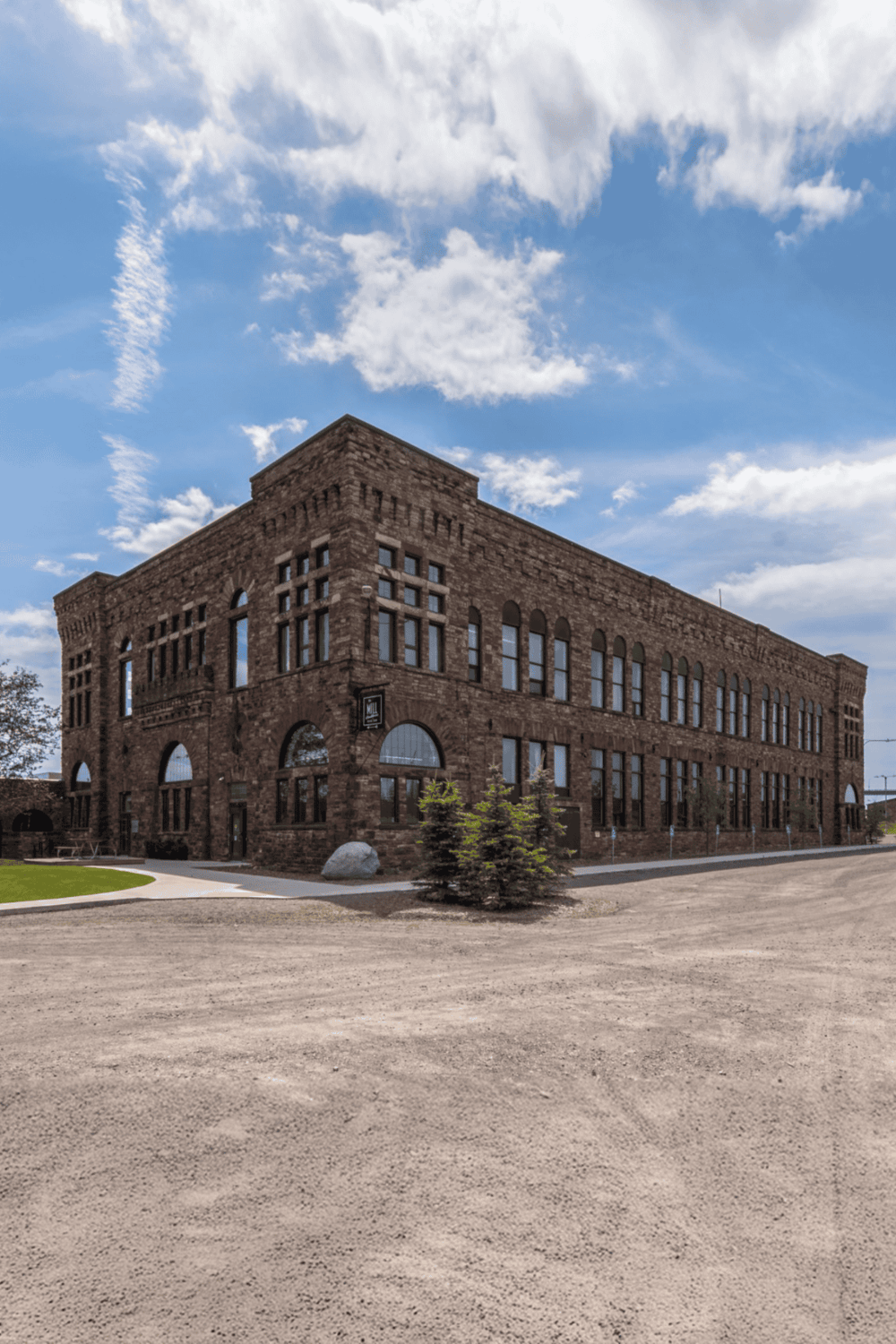 Historic brick building with large arched windows under a blue sky with clouds.