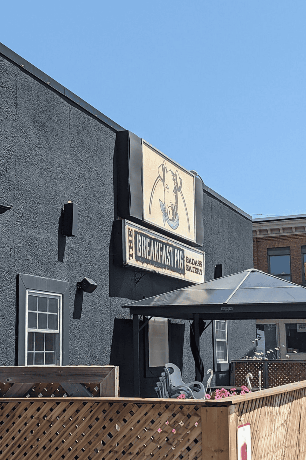 Outdoor restaurant patio with black building wall, sign for The Breakfast Pig, and outdoor seating area.