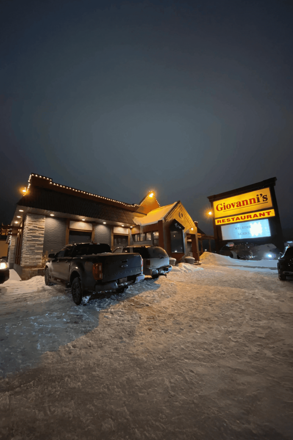 Cozy restaurant exterior illuminated at night in snowy setting, inviting guests for dining.