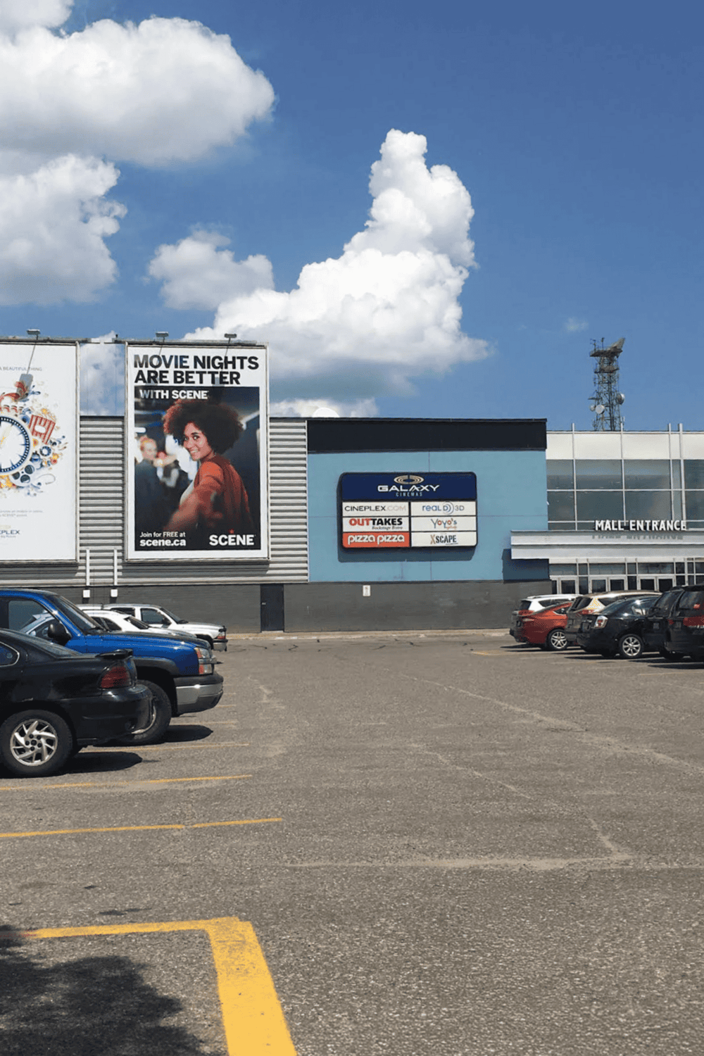 Movie theater parking lot with large billboard, colorful signage, and surrounding cars.