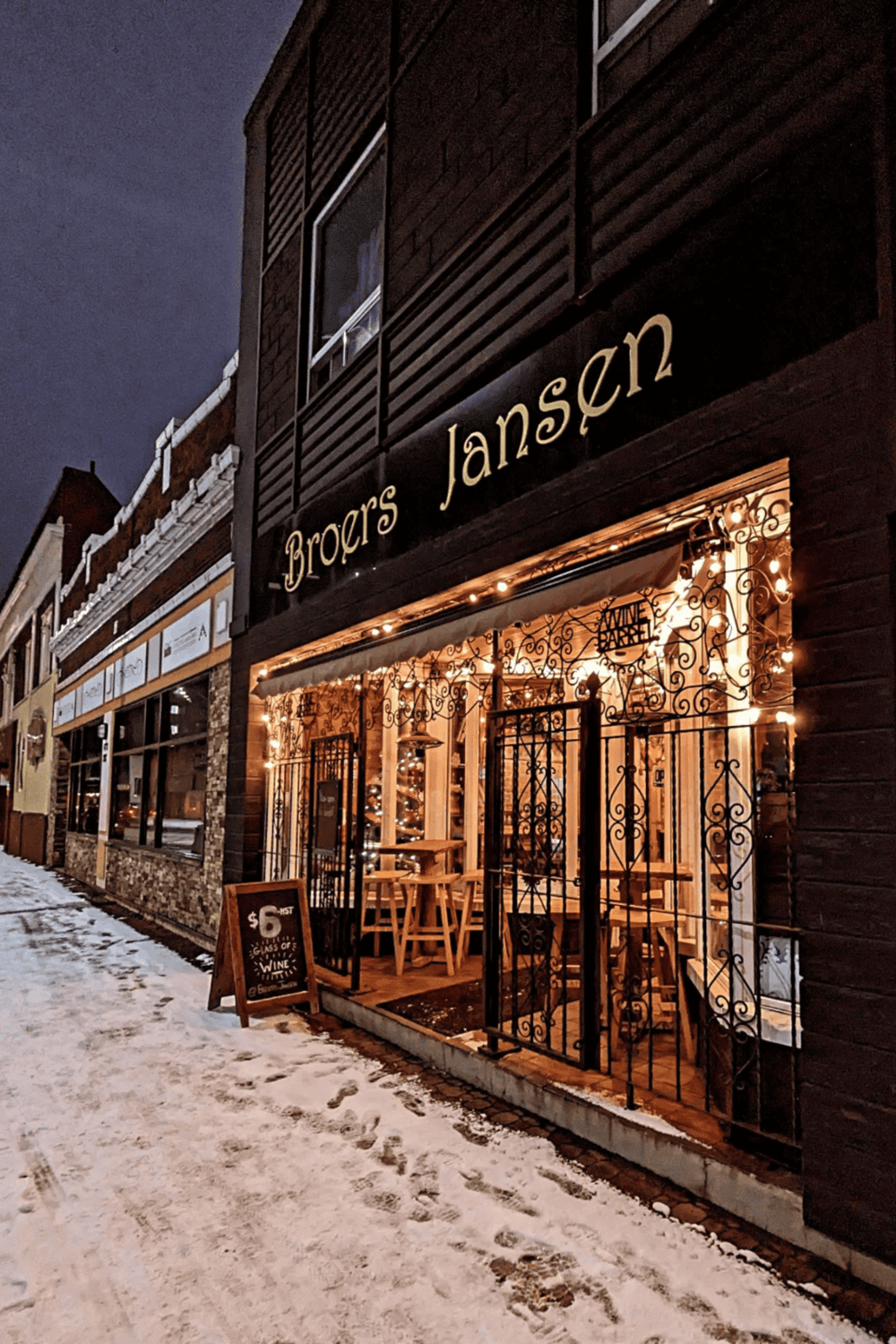 Cozy wine bar with outdoor seating at Broer's Jansen, illuminated storefront, winter night scene.