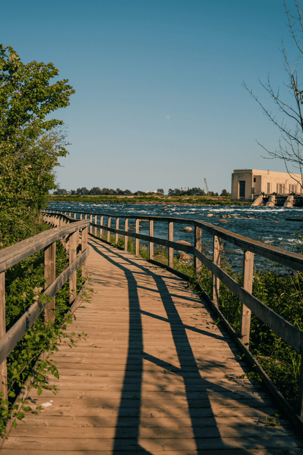 Scenic riverwalk with wooden pathway along the water, under clear blue sky.