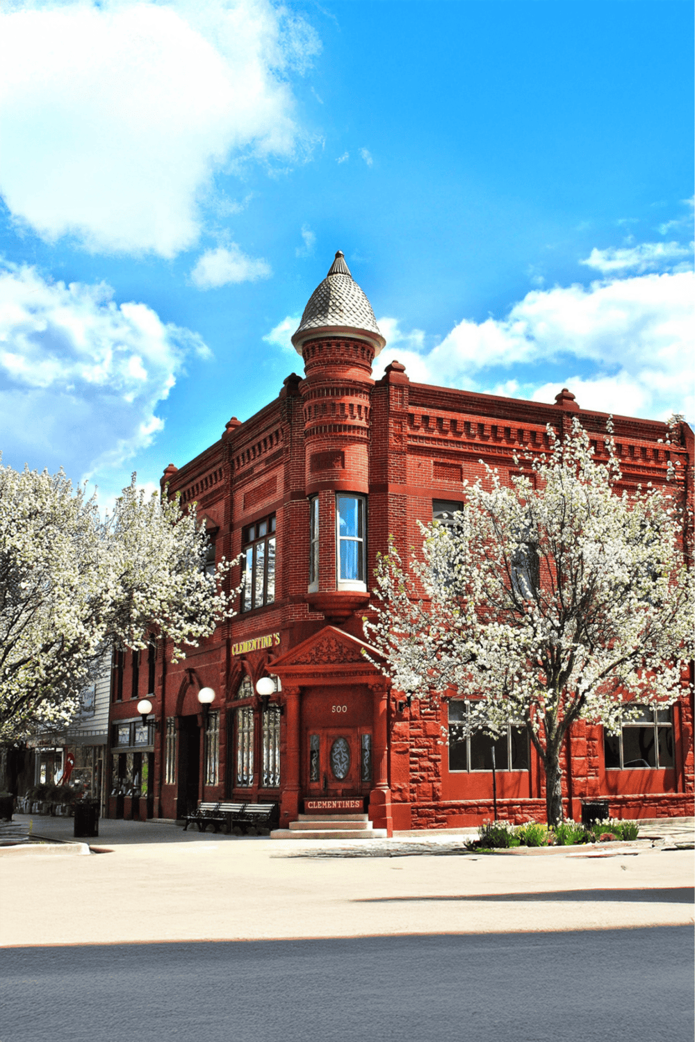 Red historic building with blooming trees and bright blue sky, featuring Quest for Directions storefront.