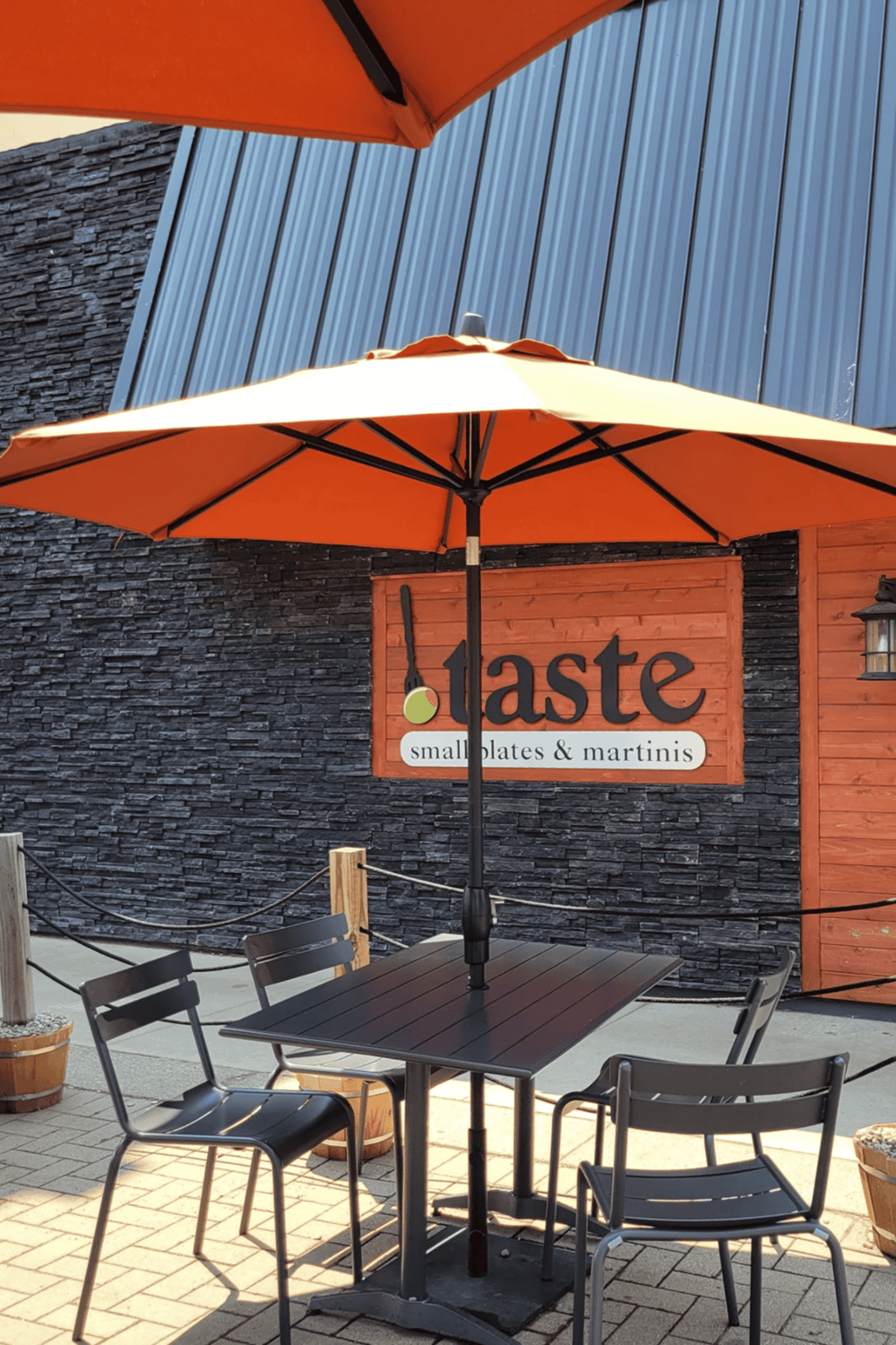 Cozy outdoor dining area with orange umbrellas, black chairs, and a restaurant sign for "Taste".