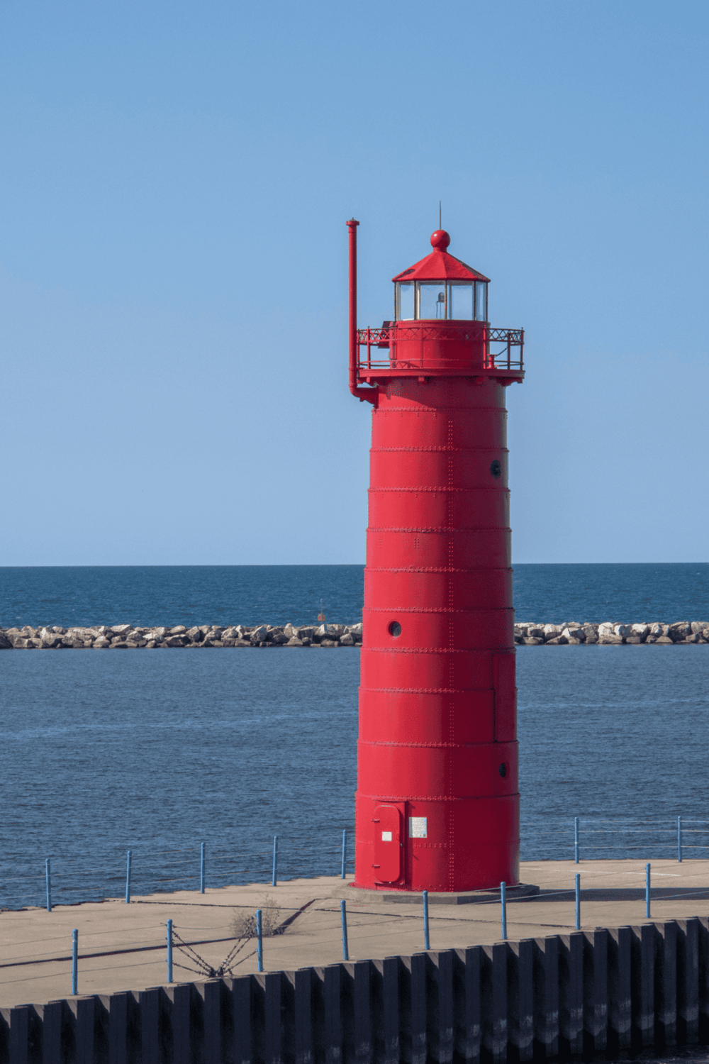 Lighthouse on a calm seaside with a breakwater in the background, symbolizing navigation and travel.