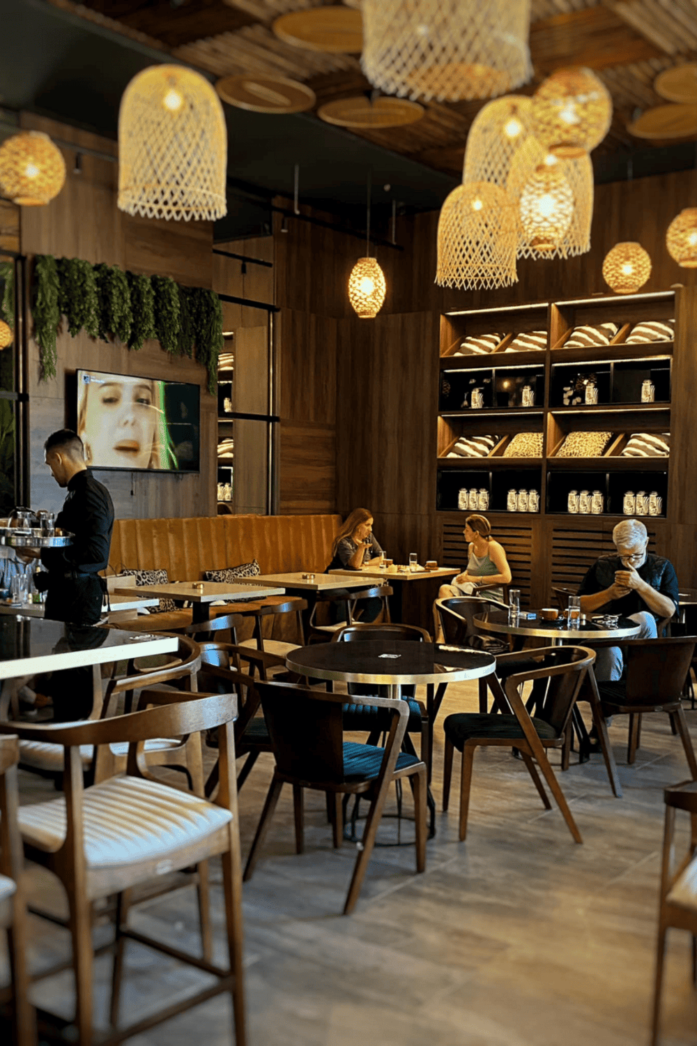 Cozy modern restaurant interior with wooden decor, ambient pendant lighting, and customers enjoying meals.