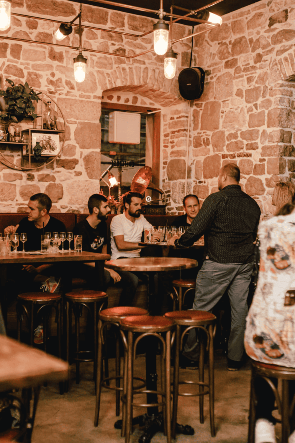 Cozy restaurant interior with rustic stone walls, warm lighting, and group of friends enjoying drinks.