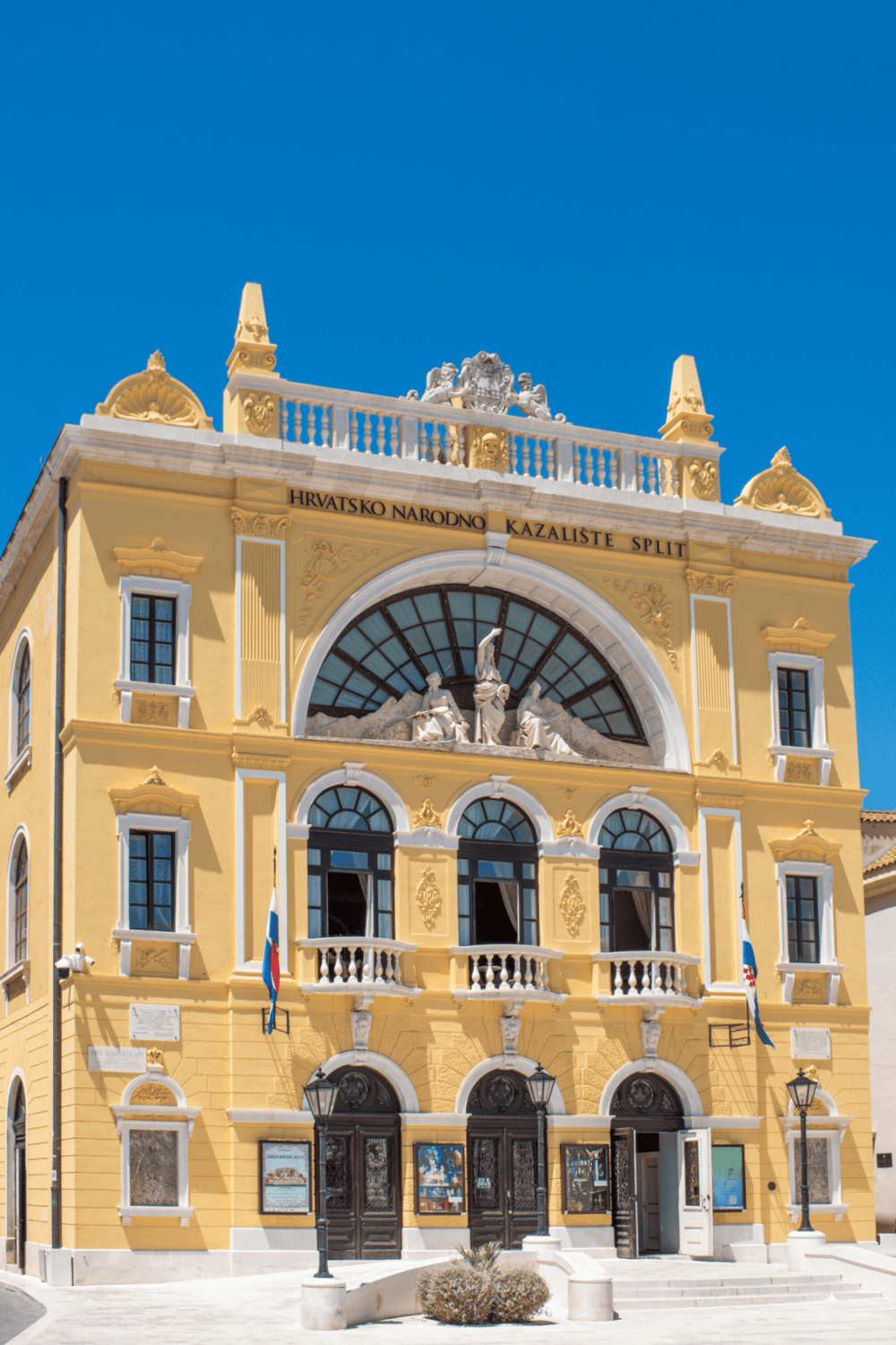 Colorful historic building with Croatian flag, ornate architecture, and clear blue sky, representing Croatian cultural heritage and city landmarks.