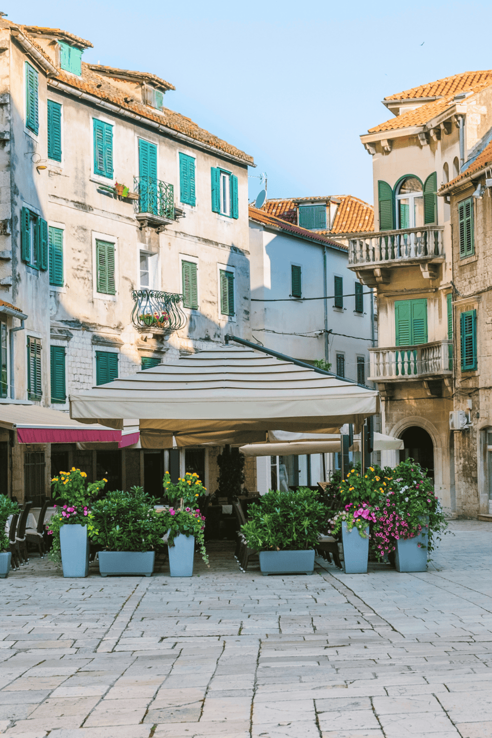 Charming European street with colorful buildings, outdoor café, and vibrant flower planters.