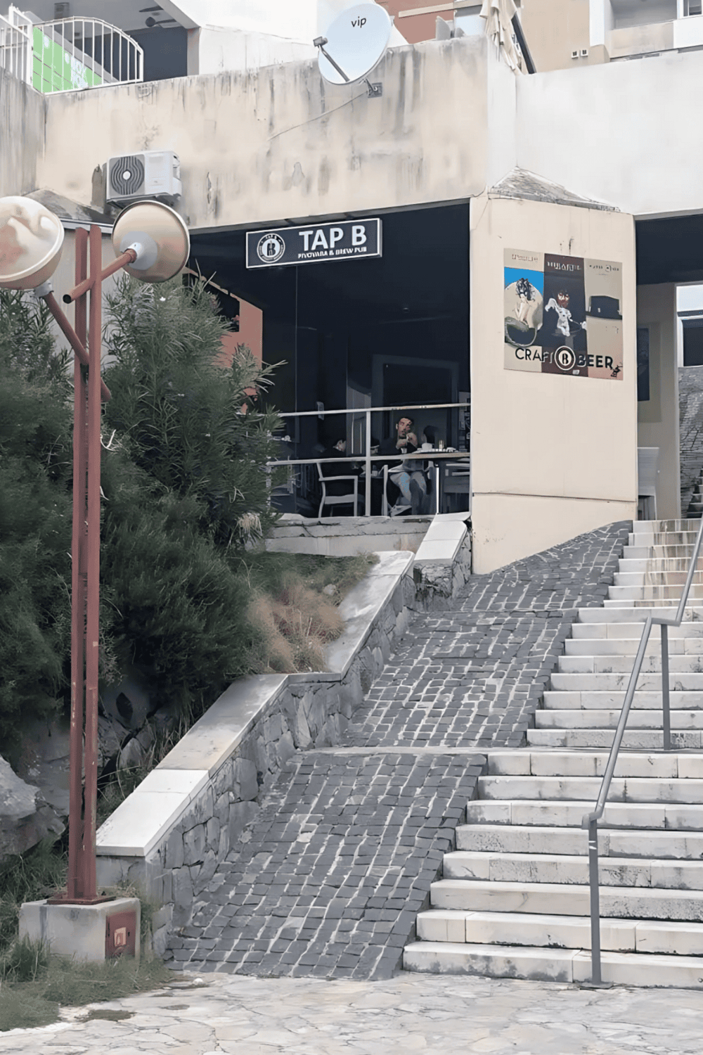 Outdoor bar and craft beer restaurant with stairs and seating area, located in a modern urban setting.