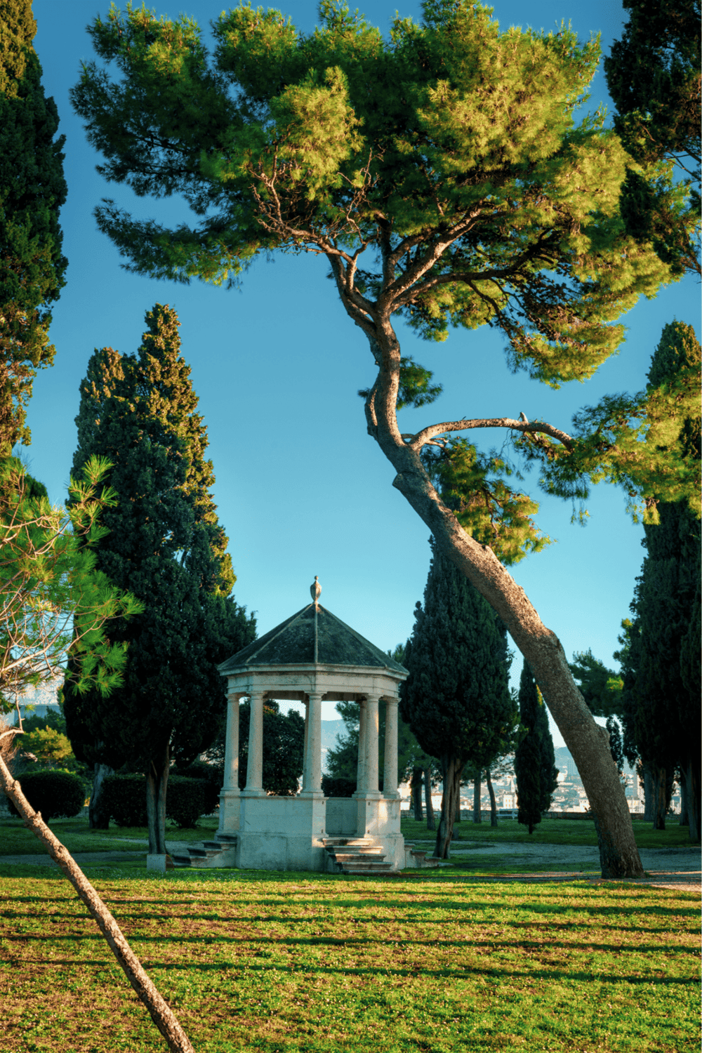 Serene park with a white pavilion, tall trees, and lush greenery in a peaceful outdoor setting.