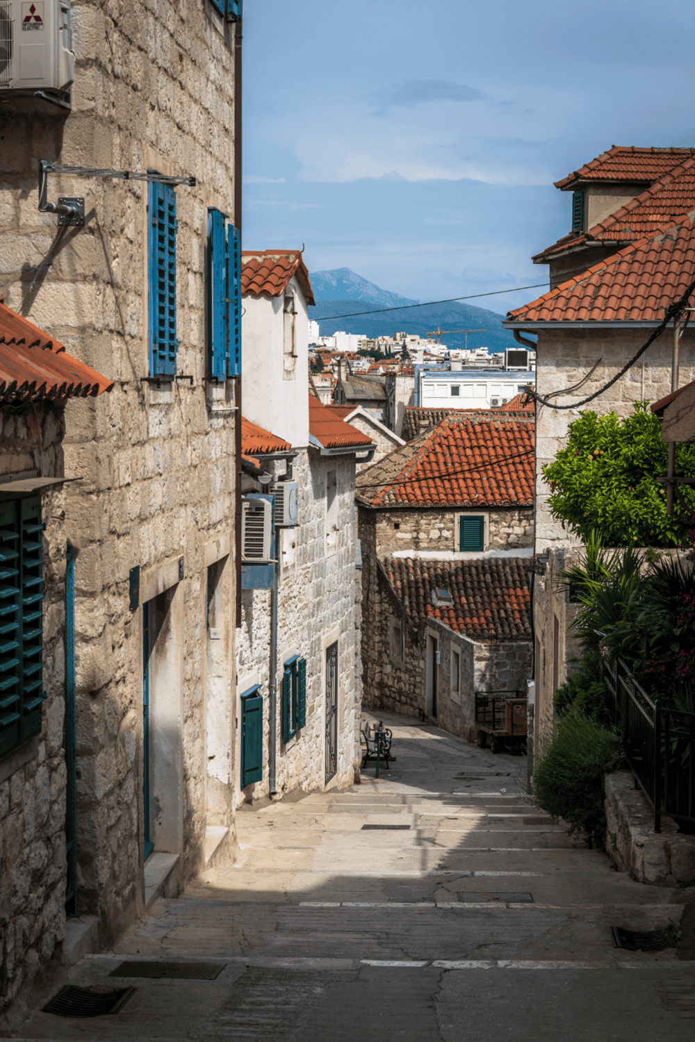Stone alleyway in historic Mediterranean town with red tile roofs and mountain view.