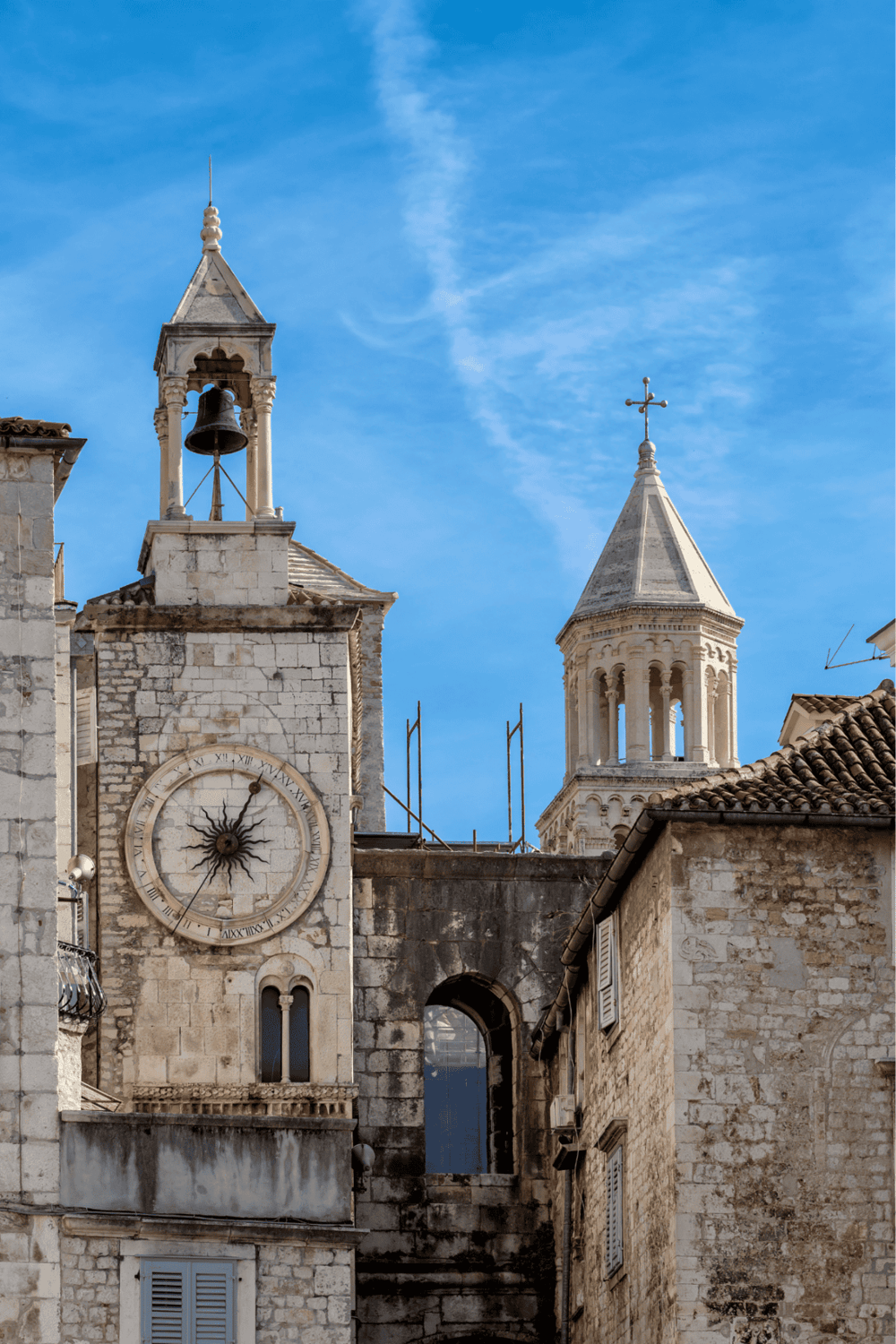 Ancient stone church with clock tower, bell, and Cross, under blue sky in historic European city.