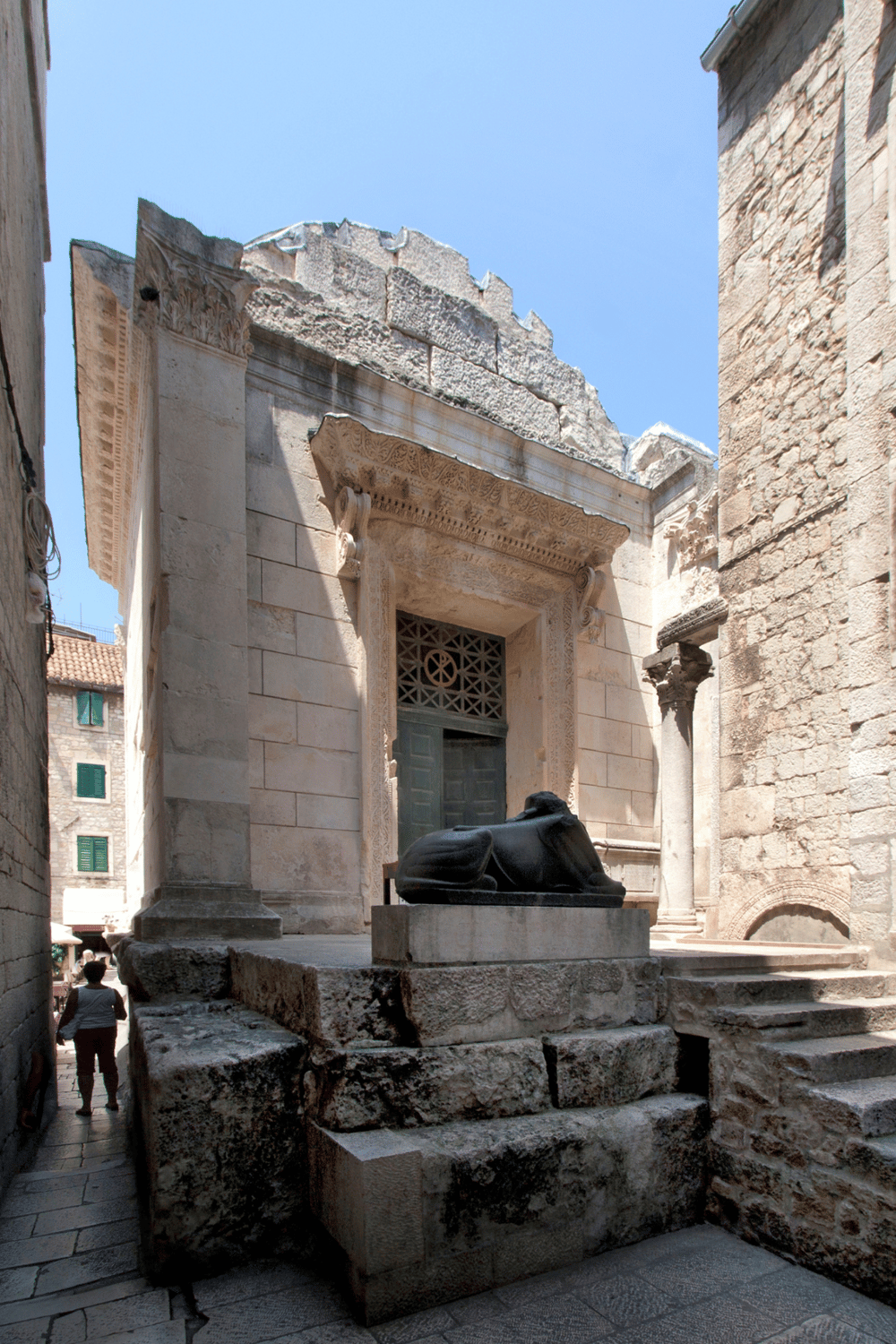 Ancient historic church facade in Dubrovnik, Croatia with carved detailing and a nearby reclining sculpture.