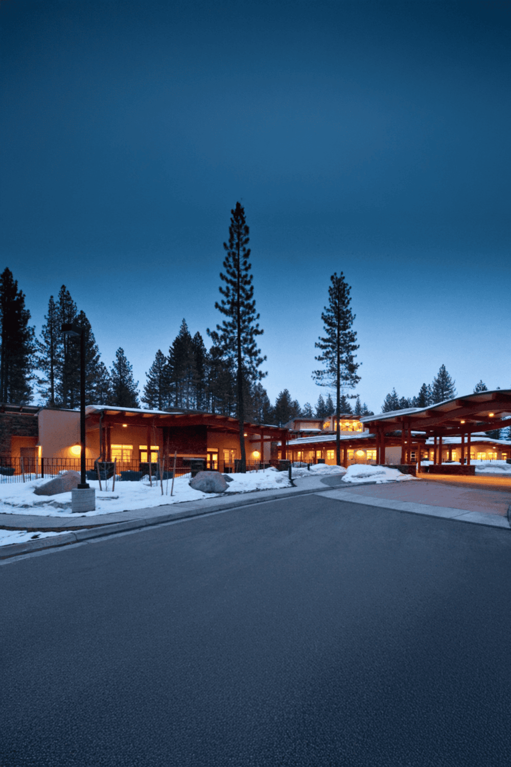 Secluded mountain lodge with snow-covered grounds and tall pine trees at dusk.