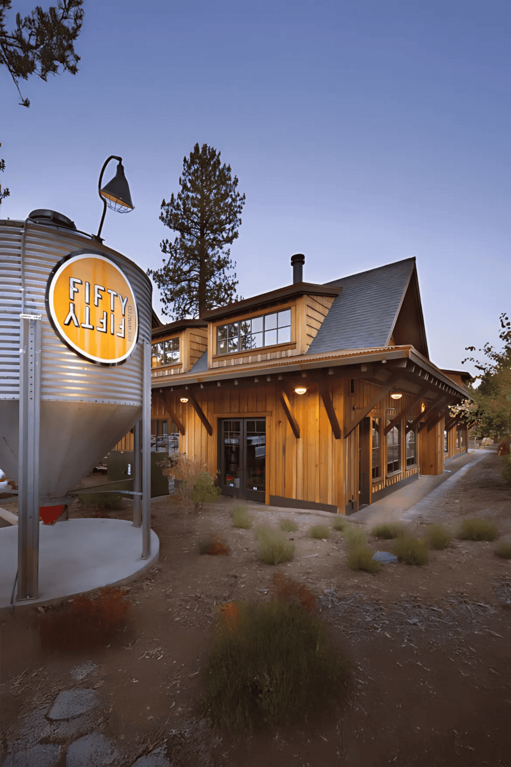 Modern rustic restaurant with wooden exterior, angled roof, and outdoor lighting, featuring the Fifty Fifty logo sign, perfect for dining and socializing.