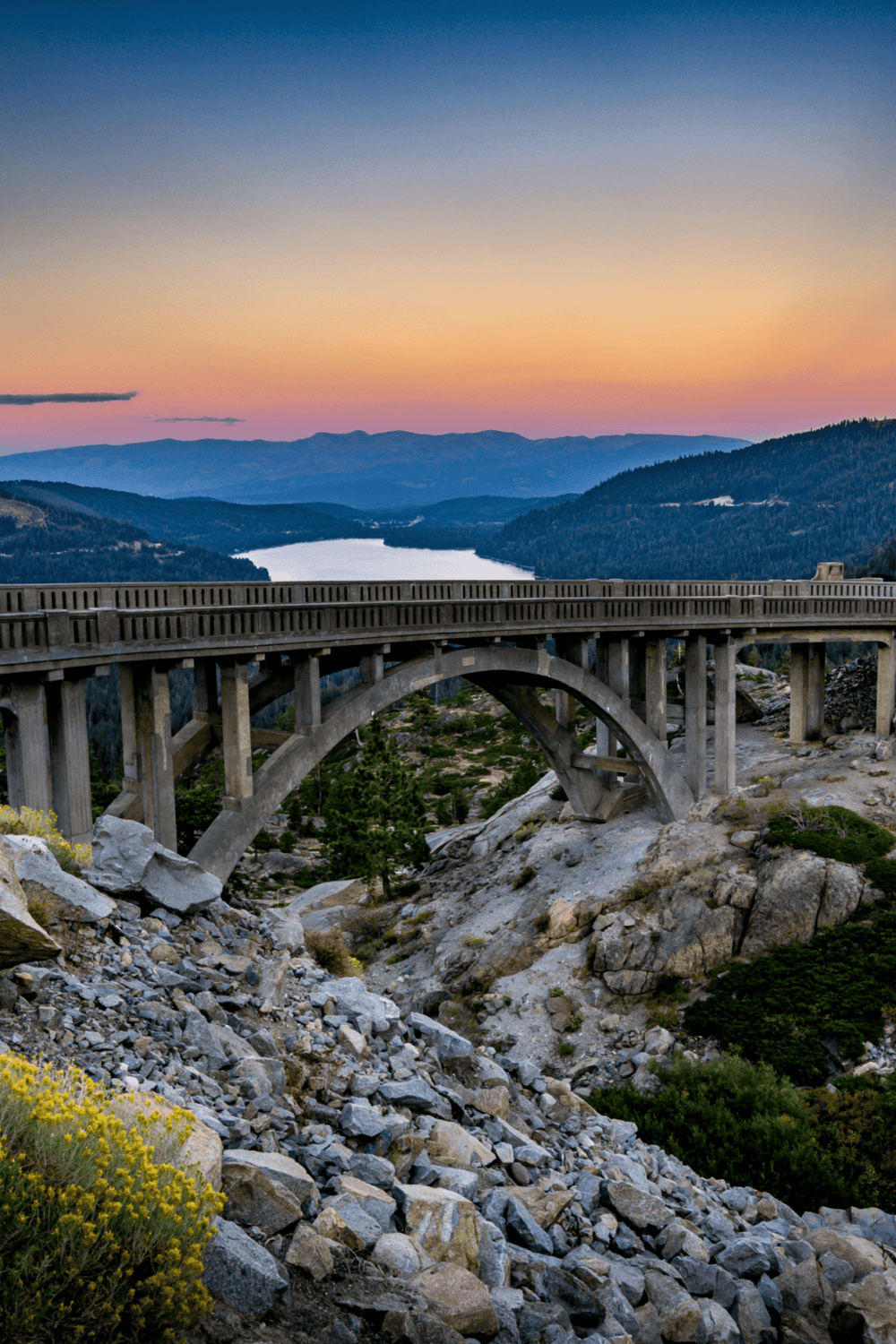 Raging Waters Scenic Bridge over Rocky Terrain with Mountain View in the Distance during Sunset.