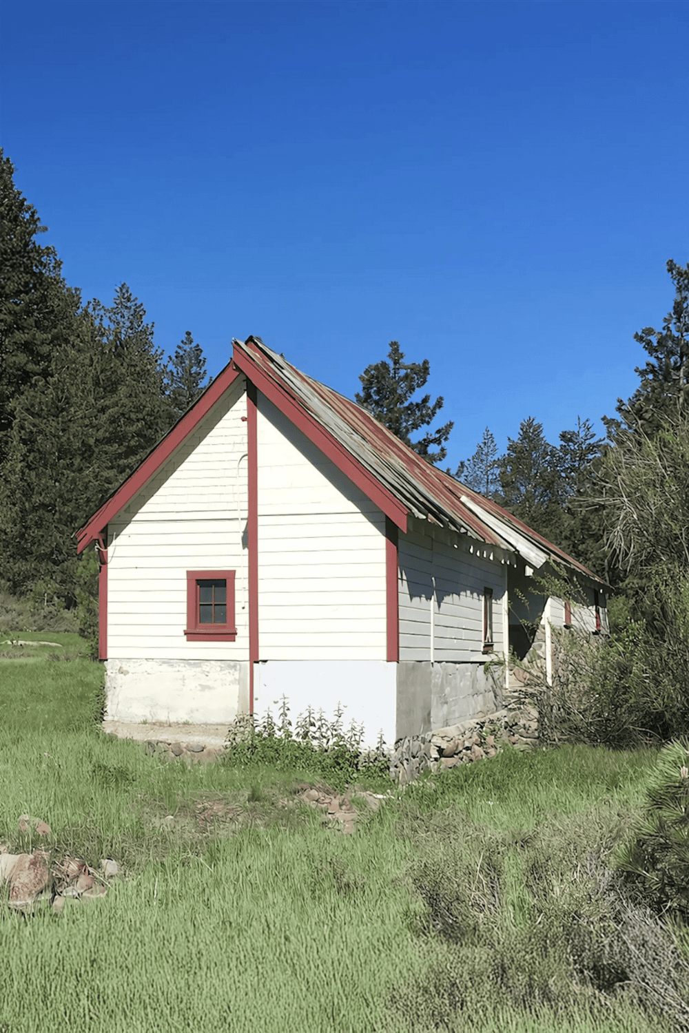 1. Abandoned white house with red trim in a rural setting under blue sky.