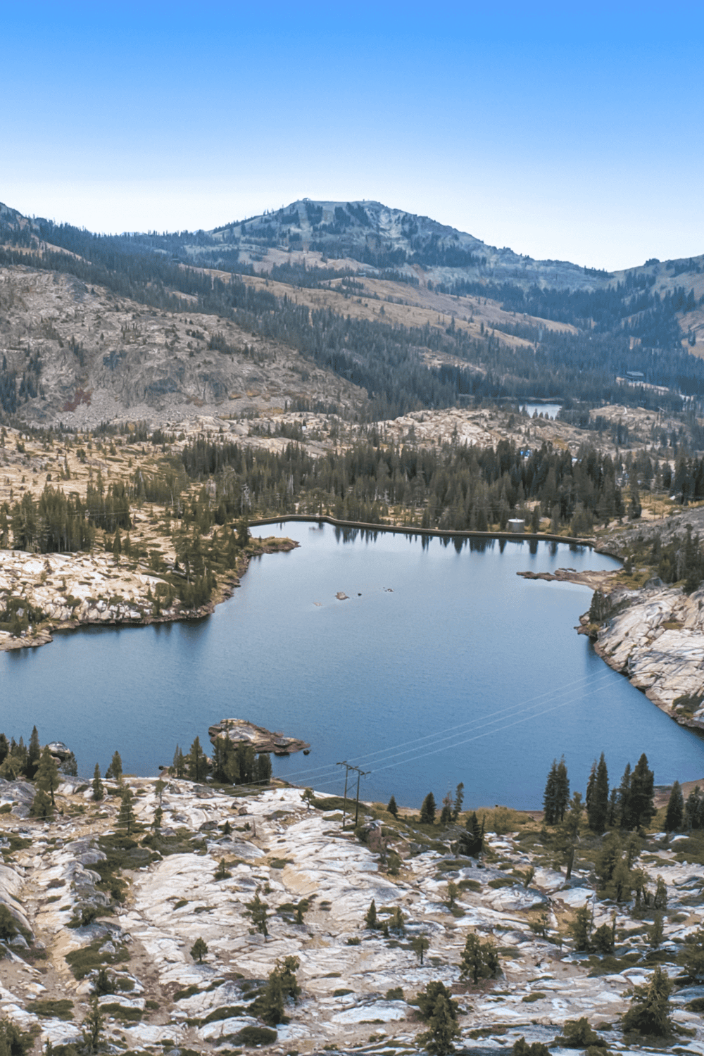 Serene mountain lake with surrounding forest and rocky terrain, perfect for hiking and outdoor adventures.