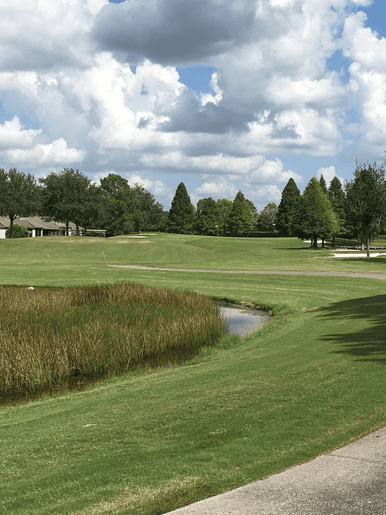 Rolling golf course with lush green fairways and trees under a partly cloudy sky.