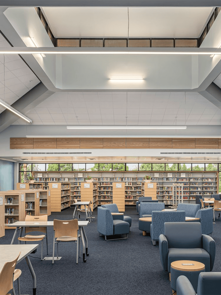 Bright modern library interior with bookshelves, seating, and large windows for a comfortable reading environment.
