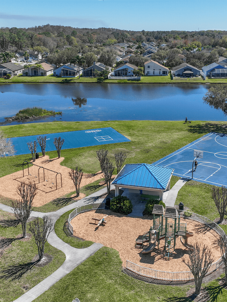 Aerial view of a lakeside community with playground, tennis courts, and walking paths, perfect for outdoor recreation.