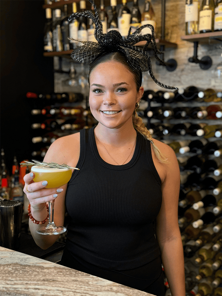 Elegant woman bartender with Halloween headpiece holding cocktail at wine bar.